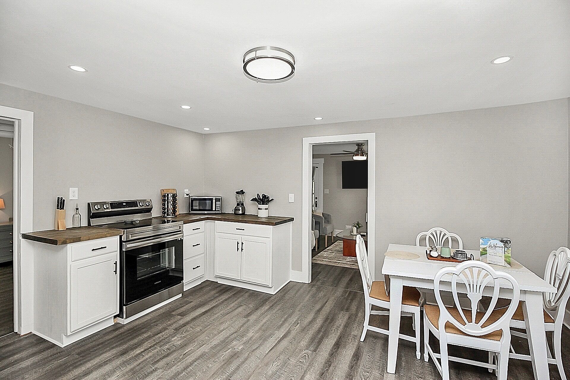 A compact kitchen with white cabinets, a microwave, a stove, and a dining area with a table and chairs.
