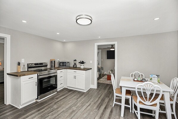 Cocina compacta con armarios blancos, microondas, estufa y comedor con mesa y sillas.