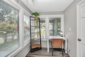 Habitación de esquina con ventana, escritorio, silla y planta.