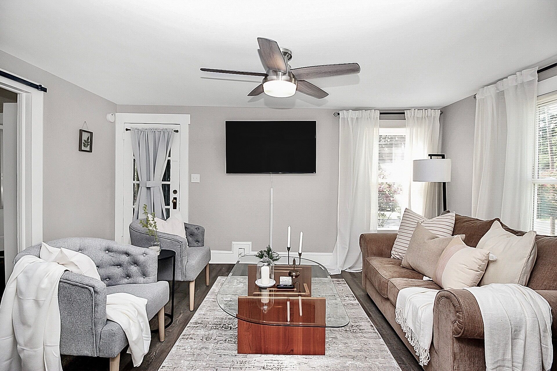 Ein Wohnzimmer mit Deckenventilator, einem Flachbildfernseher, einem grauen Sofa, einem braunen Sofa und einem Couchtisch.