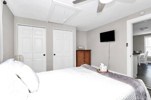 Un dormitorio con cama, armario, televisor y escritorio con silla.