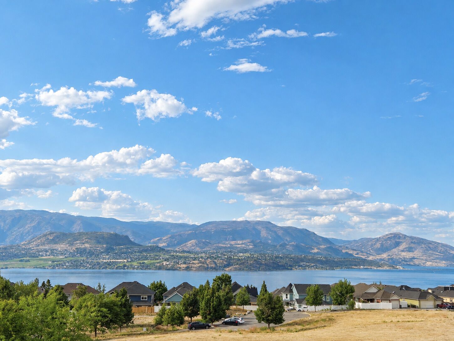 Un quartier résidentiel avec des maisons, un lac et des montagnes en arrière-plan.