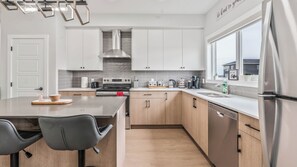 A modern kitchen with white cabinets, stainless steel appliances, and a large window. - Luxurious  4-bedroom house w/ Free Banff Pass (Northeast)