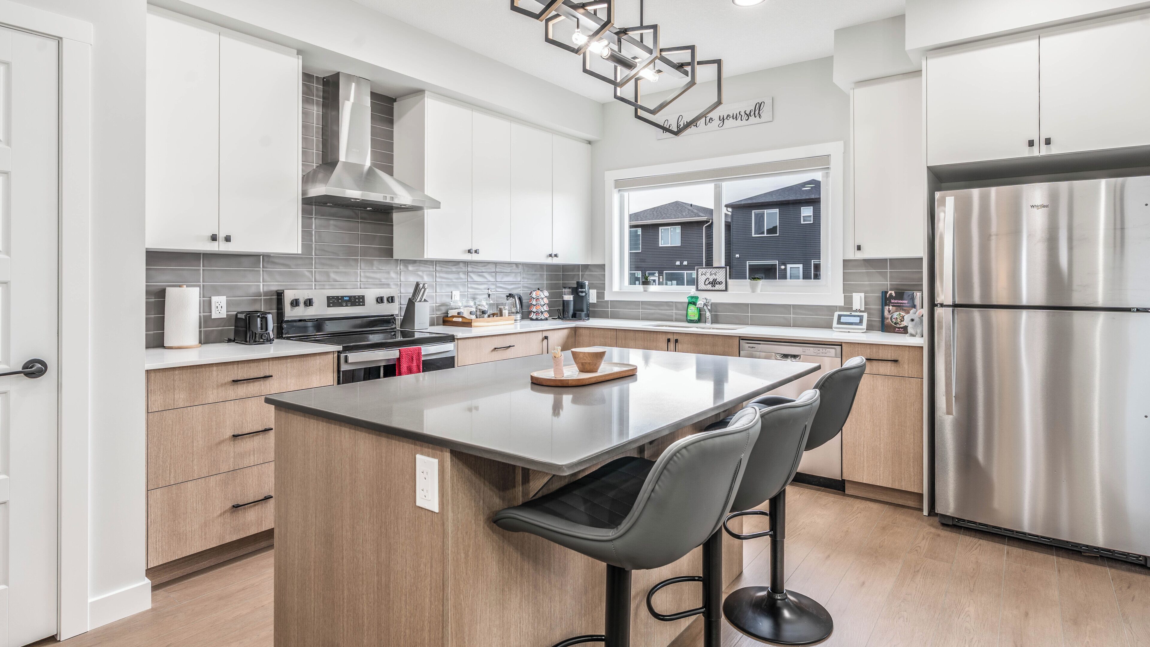 A modern kitchen with a central island, stainless steel appliances, and a view of the outside.