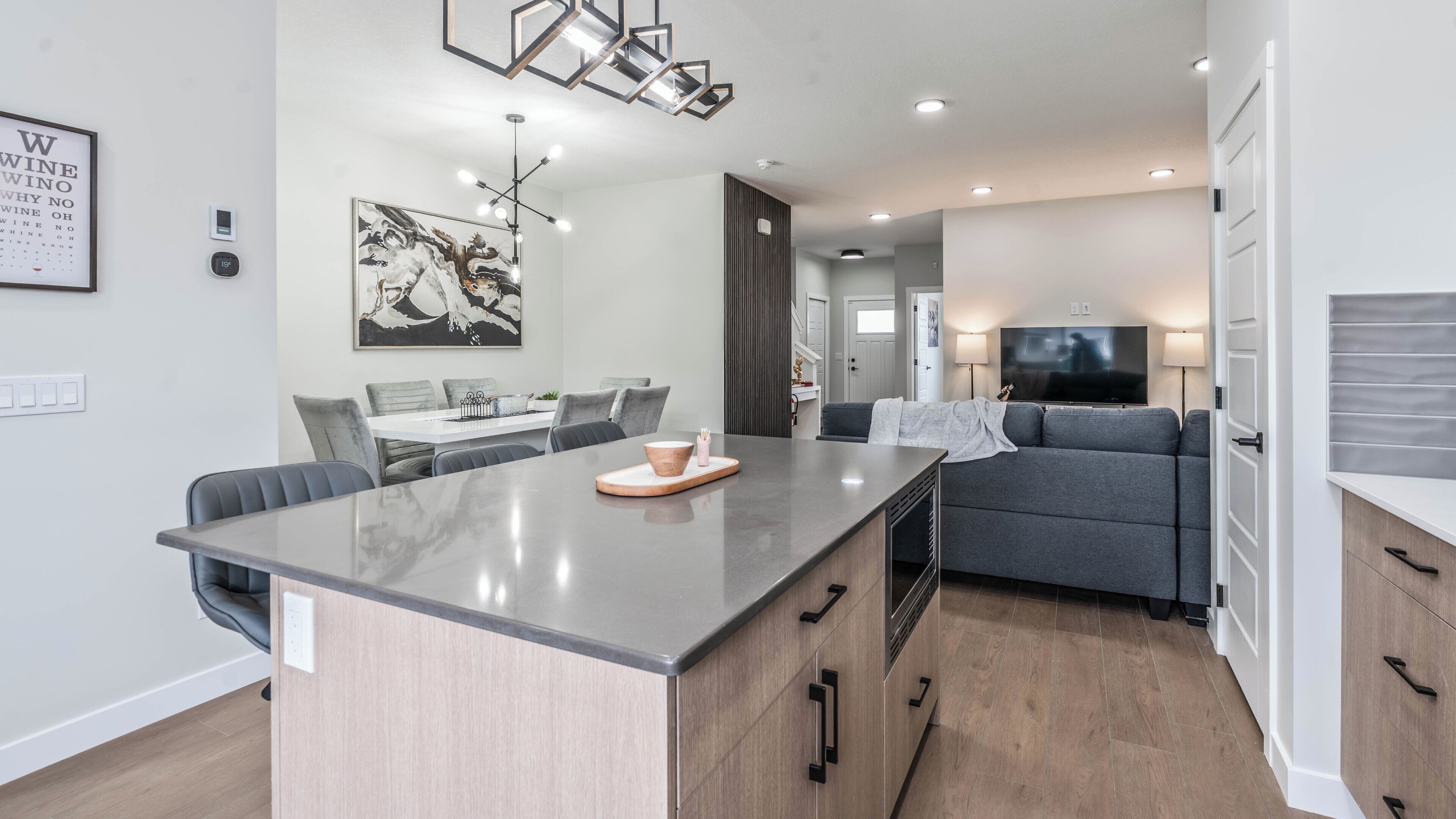 A modern kitchen with a central island, dining area, and a living space with a sofa and TV.