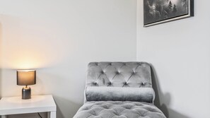 A room with a grey upholstered armchair, a white side table with a lamp, and a framed picture on the wall. - Luxurious  4-bedroom house w/ Free Banff Pass (Northeast)