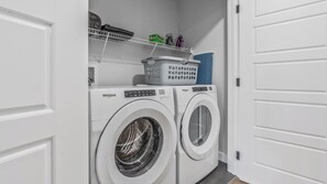 A laundry room with two Whirlpool washing machines, a shelf with laundry baskets and cleaning supplies. - Luxurious  4-bedroom house w/ Free Banff Pass (Northeast)