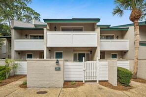Um edifício residencial de vários andares com portão de entrada, placa de identificação visível e uma pequena área ajardinada.