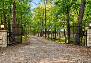 A gravel driveway leading to a gated entrance surrounded by trees. - Heated Pool | Boat Parking | Outdoor Kitchen (Broken Bow)