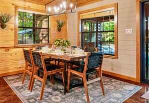 A wooden dining room with a table set for four, surrounded by chairs with dark upholstery. - Heated Pool | Boat Parking | Outdoor Kitchen (Broken Bow)