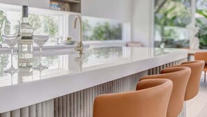 Eine moderne Küche mit einer zentralen Kochinsel, Barhocker und Blick ins Freie.