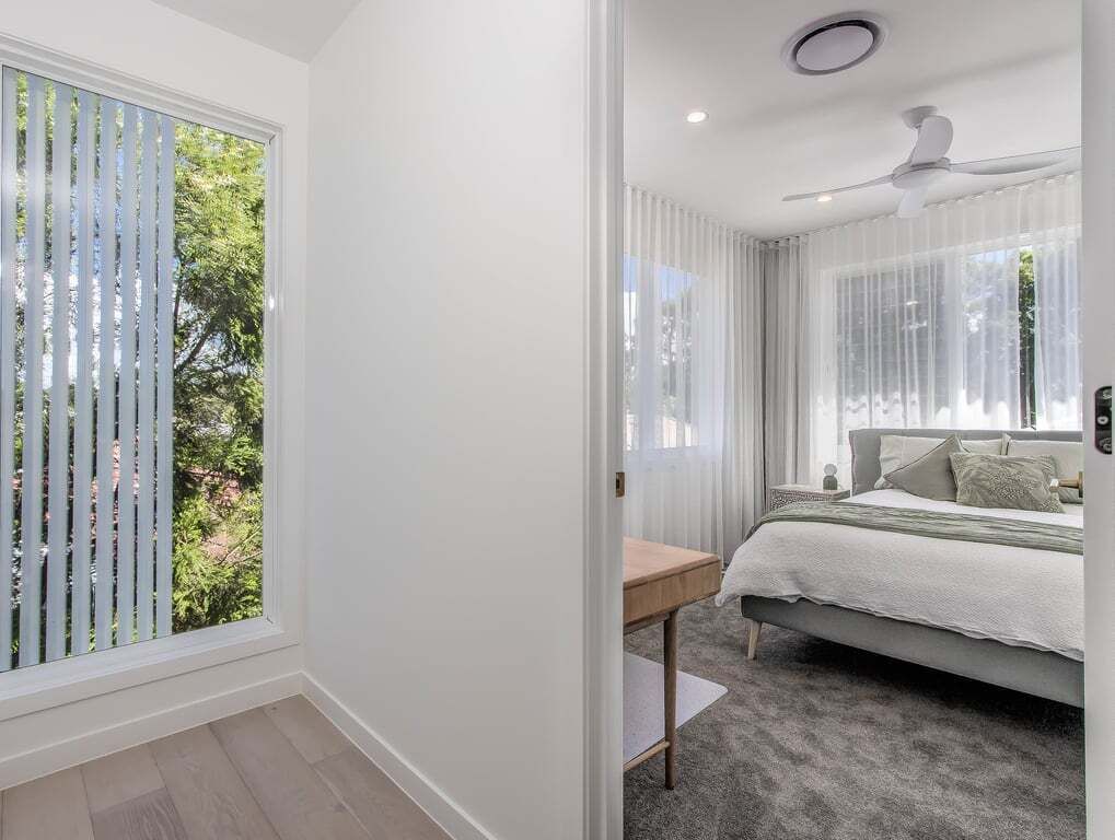 A bedroom with a bed, a bedside table, a ceiling fan, and a window with blinds.