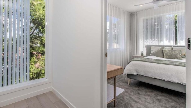 Ein Schlafzimmer mit einem Bett, einem Nachttisch, einem Deckenventilator und einem Fenster mit Jalousien.