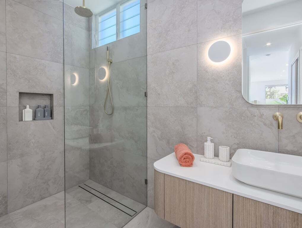 Une salle de bain moderne avec une douche à parois de verre, un lavabo blanc et un miroir.