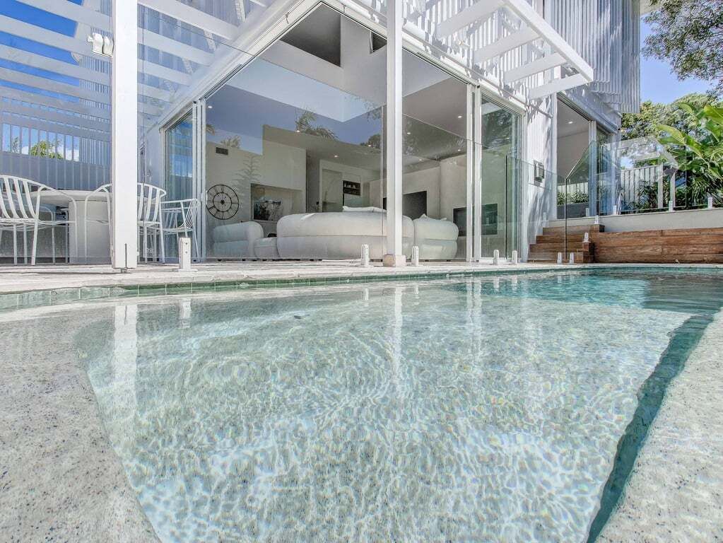 A modern hotel room with a glass wall, a bed, and a view of the pool.