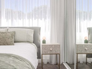 Een slaapkamer met een bed, twee nachtkastjes en een raam met dunne gordijnen.