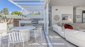 Eine moderne Außenpatio mit Esstisch und Stühlen, einem weißen Sofa und einem durch eine offene Tür einsehbaren Küchenbereich.