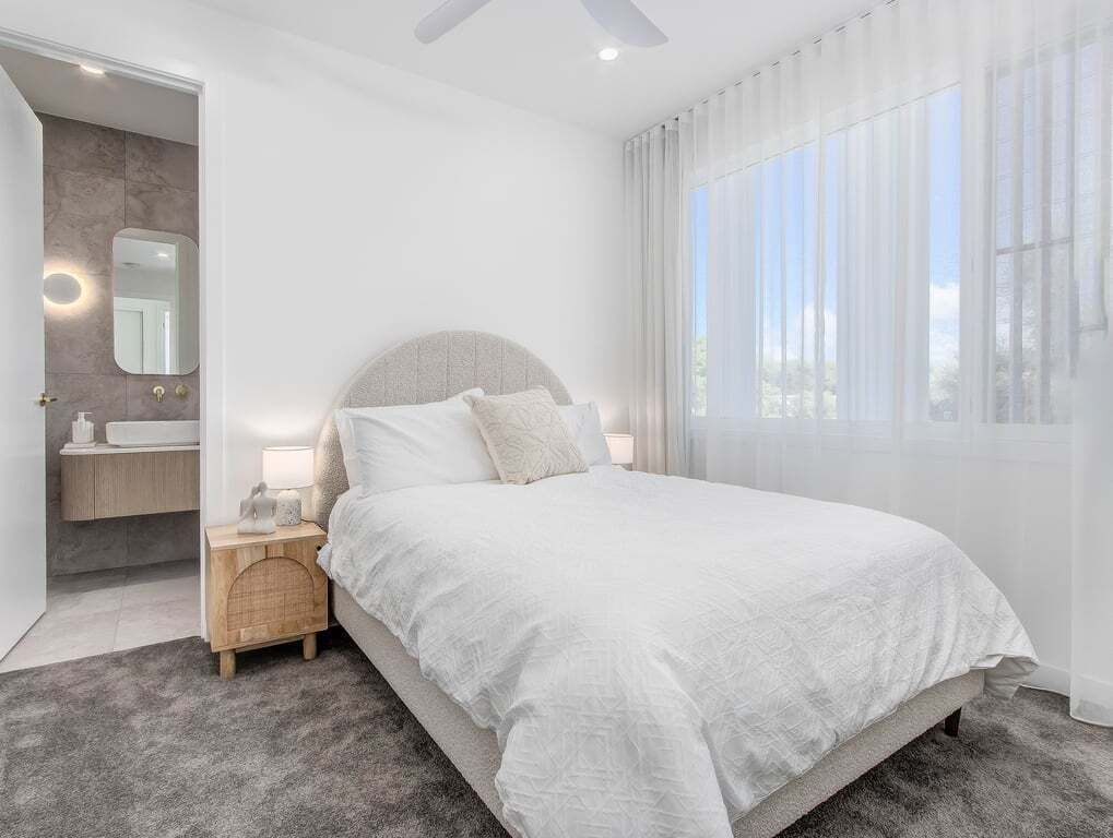 Una camera da letto moderna con un letto, un comodino e un bagno visibile attraverso una porta aperta.