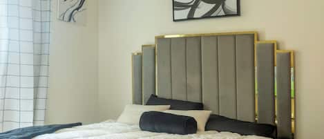 A bedroom with a bed, a ceiling fan, a wall-mounted abstract painting, and a window with a curtain.