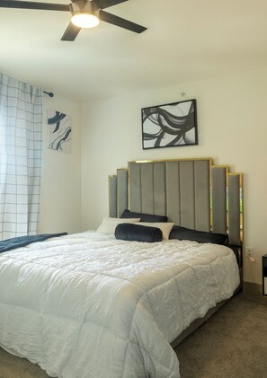 A bedroom with a bed, a ceiling fan, a wall-mounted abstract painting, and a window with a curtain. - Skyline-View, 2BR, 2.5Bt, Pool, Gym& Free Parking (Dallas)