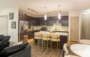 A modern kitchen with stainless steel appliances, dark wood cabinets, and a central island with bar stools. - Skyline-View, 2BR, 2.5Bt, Pool, Gym& Free Parking (Dallas)