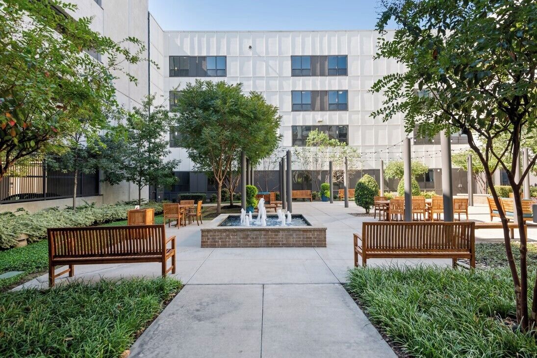 An outdoor courtyard with a central fountain, surrounded by benches and greenery.