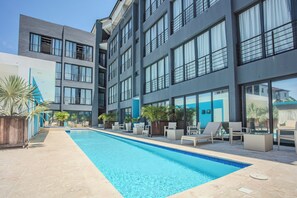 A modern hotel with a swimming pool, outdoor seating, and large windows. - Cozy 1-bedroom apartment in tranquil Sosúa with AC, Hot Water, Pool and GYM (Sosúa)