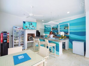 Una cocina con barra, refrigerador, máquina de café y televisor.