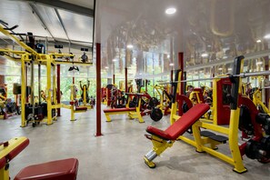 Une salle de sport équipée de divers appareils d’exercice, de bancs et dotée d’un mur recouvert de miroirs.