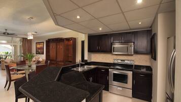 A modern kitchen with dark cabinets, stainless steel appliances, and a glass dining table.