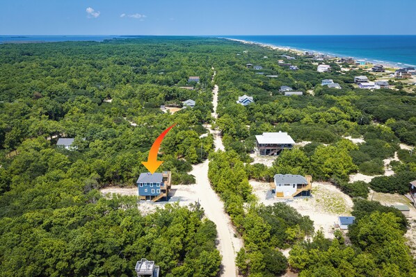 An aerial view of a coastal area with dense greenery, a clear sky, and a beach in the distance.