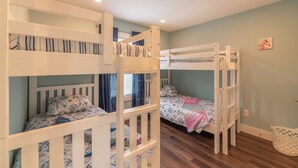 Um quarto com beliches, uma janela com cortinas e uma parede com um pequeno quadro.