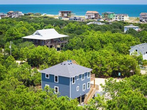 A coastal residential area with multiple houses, some with decks and balconies, surrounded by dense greenery and a view of the ocean. - The Fourth Watch - 4x4 Carova Beach, Ocean View, Brand New, Linens, Flex Stays (Carova Beach)