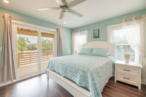 Quarto com cama, ventoinha no teto, janela com cortinas e vista para o exterior.