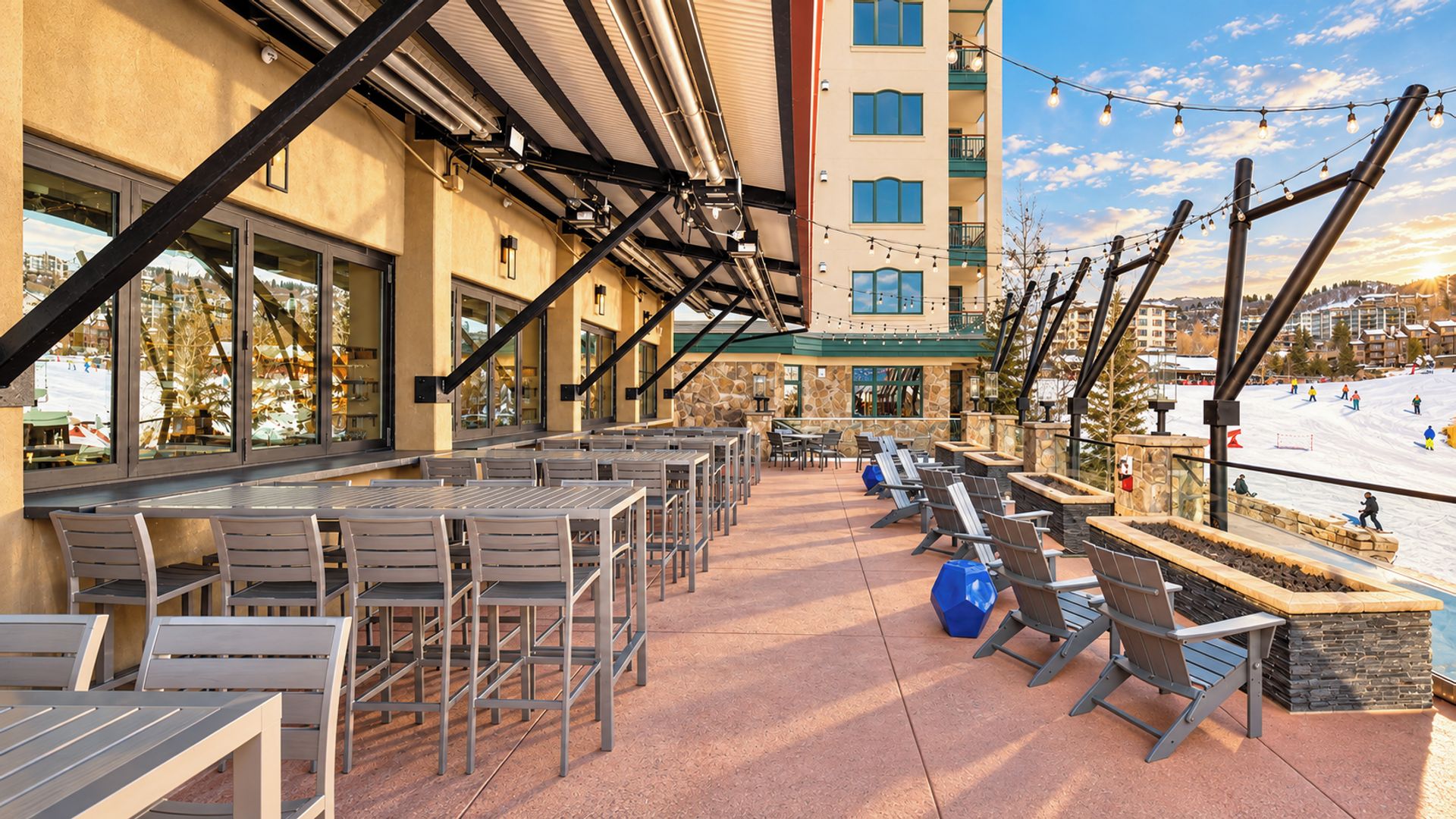 An outdoor patio with tables and chairs, a stone wall, and a view of a ski slope.