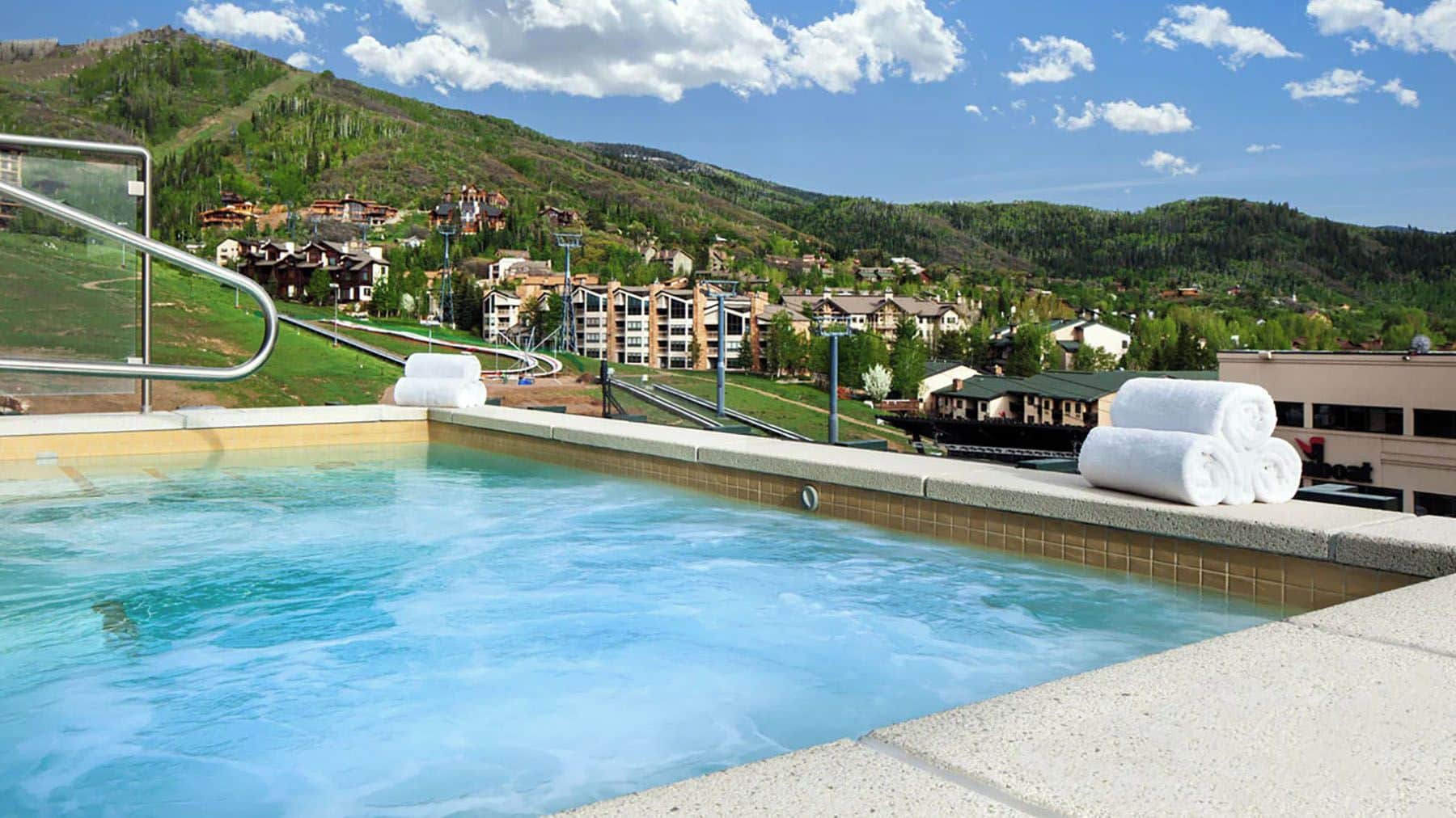 A swimming pool with a view of a hillside town, a chairlift, and a building with a 'Boat' sign.