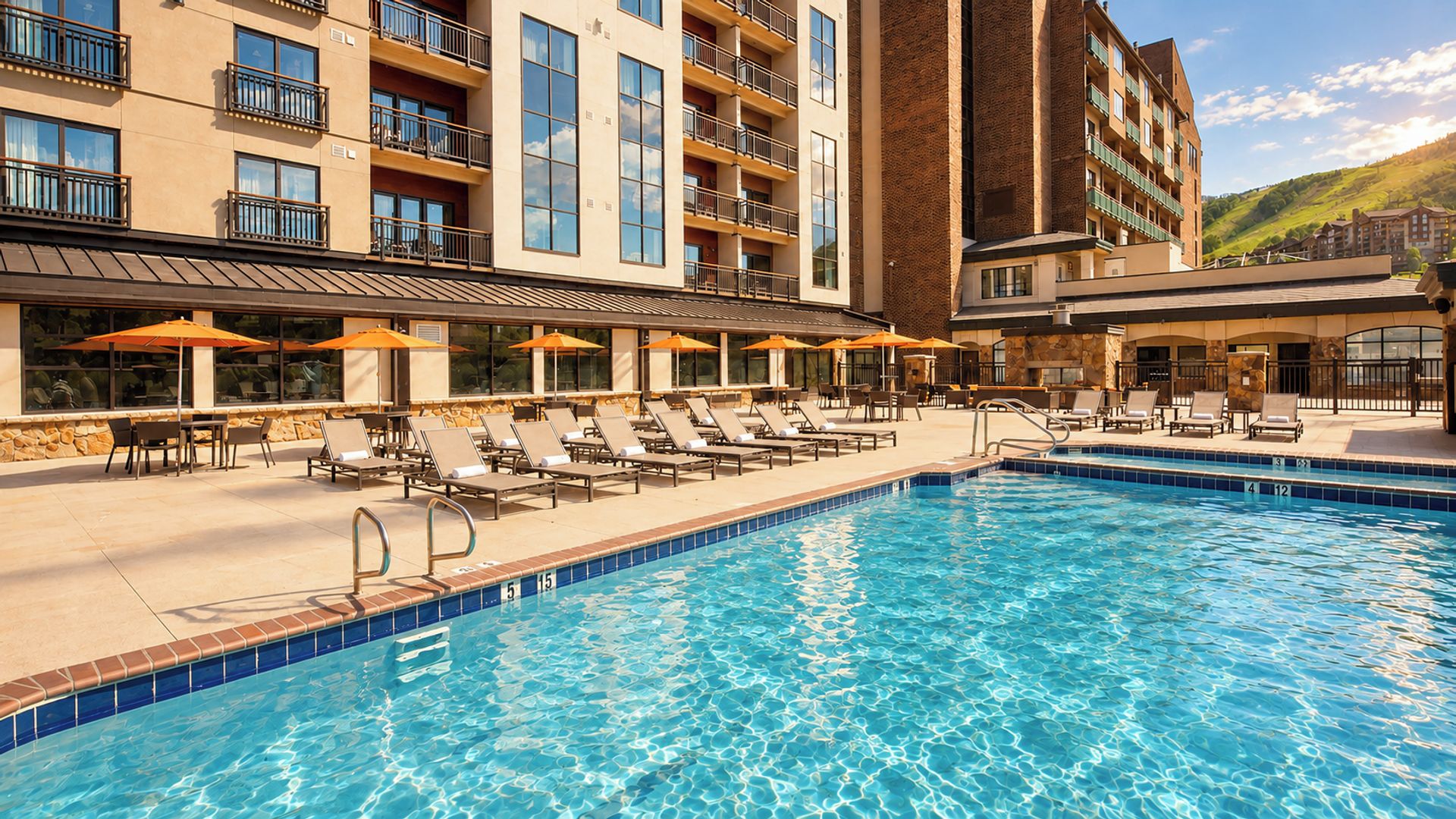 Un espace piscine d’hôtel avec des chaises longues et des parasols, une piscine à l’eau d’un bleu limpide et un bâtiment doté de nombreux balcons.