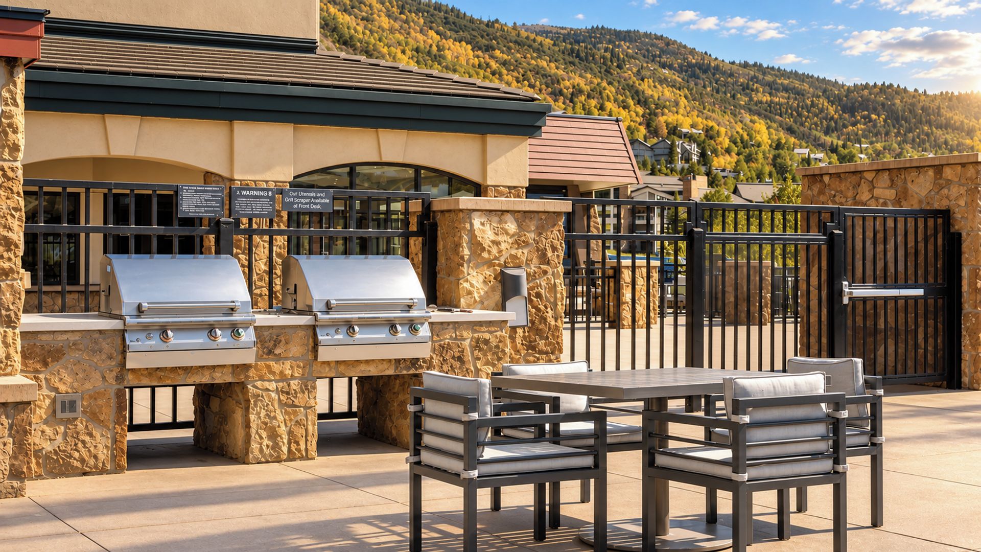 An outdoor grill area with stone pillars, a table with chairs, and a view of a mountainous landscape.