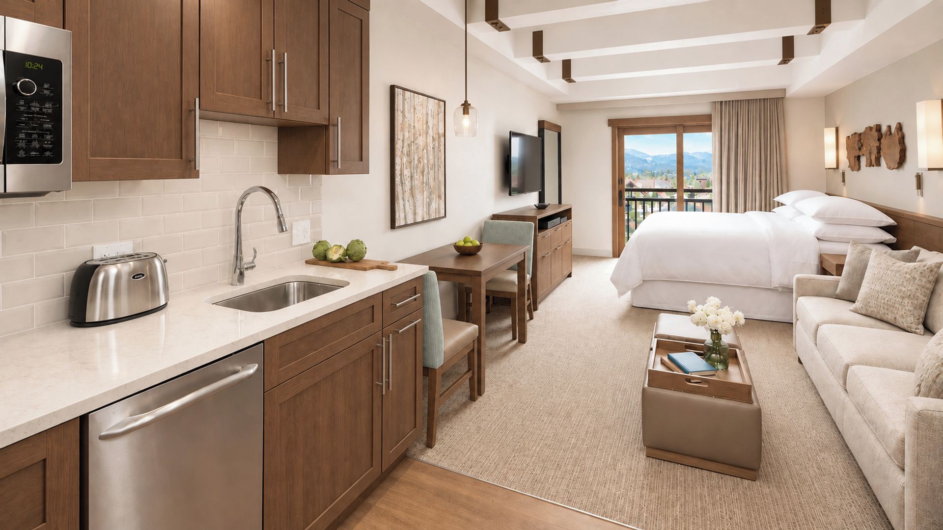 A modern hotel room with a kitchenette, a dining area, a bed, and a view of the mountains.