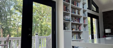 A room with a large bookshelf, a white desk, and a view of a deck with a chair.