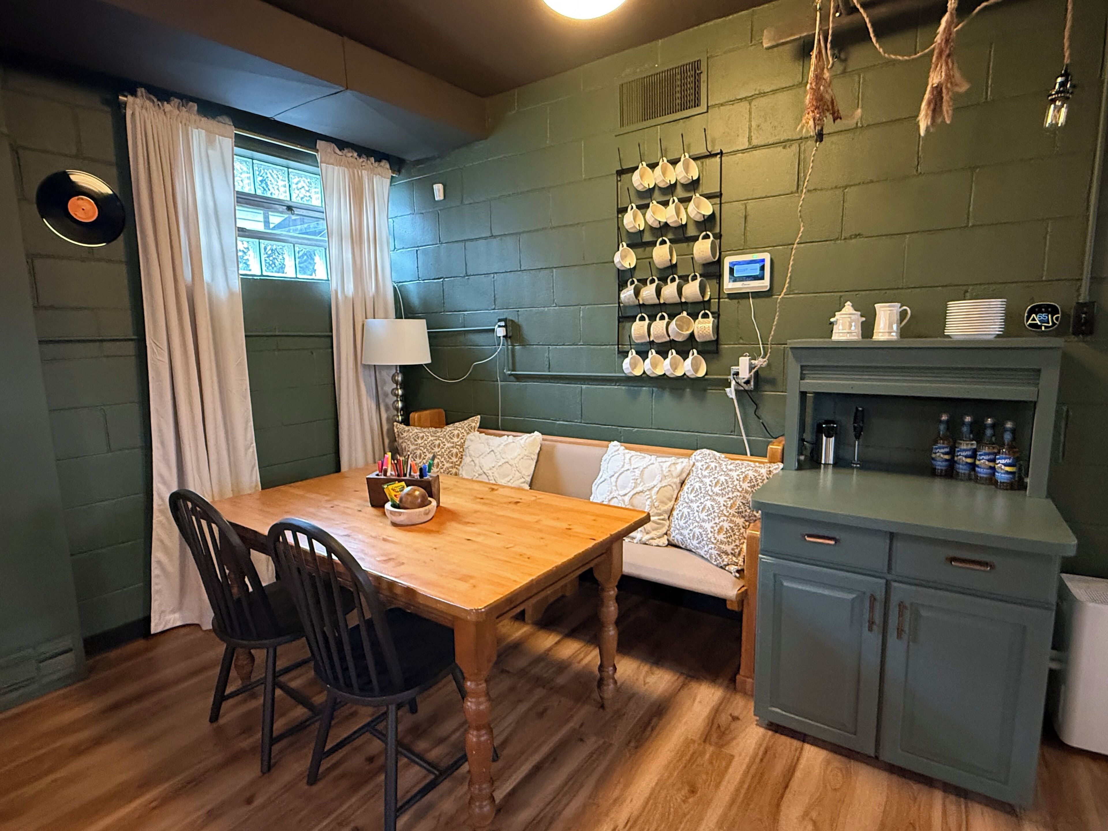 Une pièce chaleureuse avec une table à manger en bois, deux chaises, un canapé agrémenté de coussins à motifs, un porte-tasses fixé au mur et un meuble contenant des bouteilles.