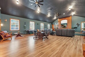 A spacious living room with a wooden floor, a large gray sectional sofa, a dining table with chairs, and a ceiling fan.