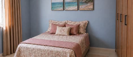 A bedroom with a bed, a window with curtains, a wall-mounted air conditioner, and a wooden wardrobe.