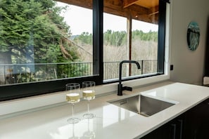 A kitchen with a large window, a stainless steel sink, and three glasses of white liquid. - Well Located | Stylish | Scenic - HS786003 (Hanmer)