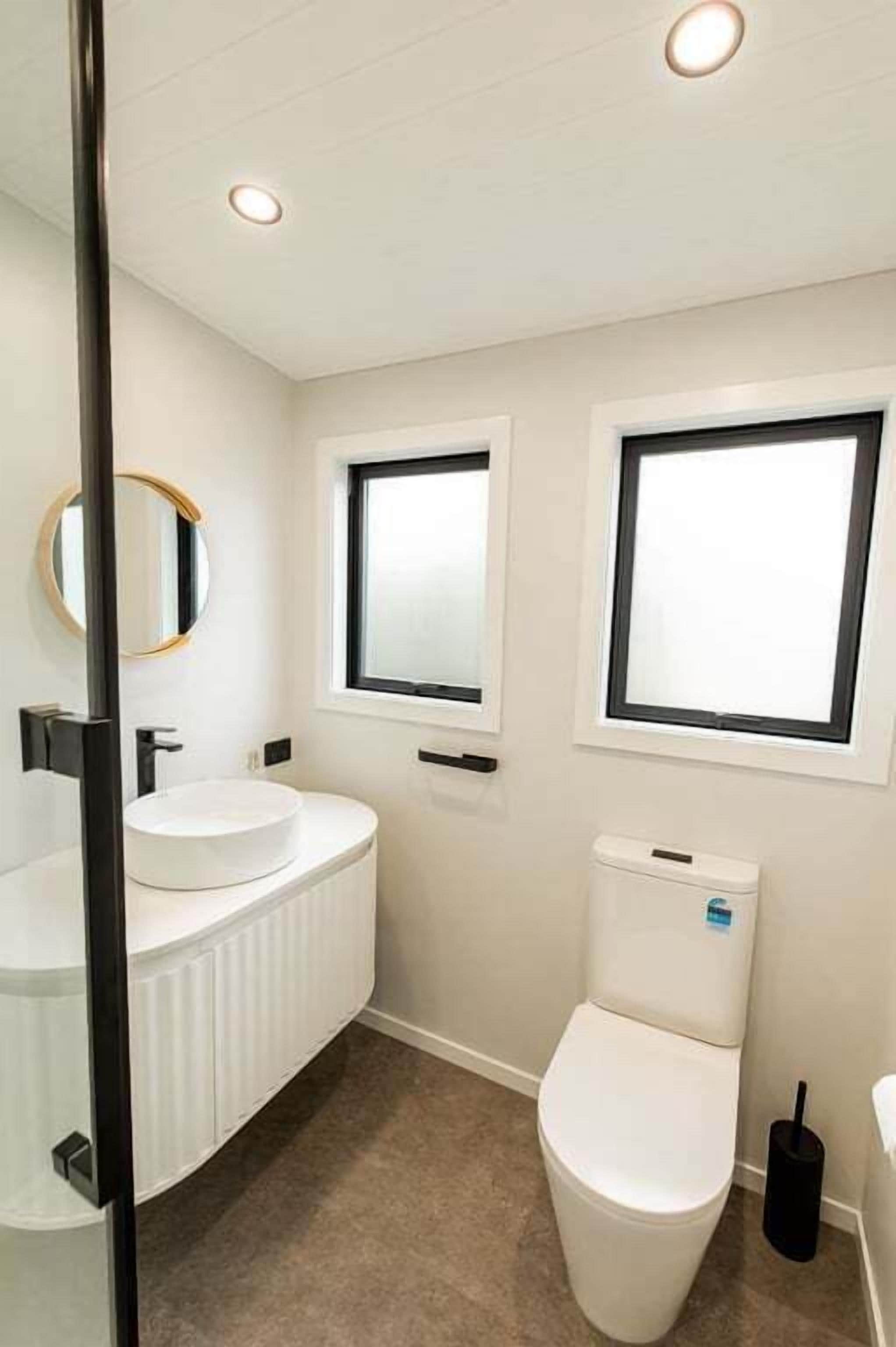 Ein Badezimmer mit Toilette, einem runden Spiegel und einem Waschbecken mit weißer Arbeitsplatte.