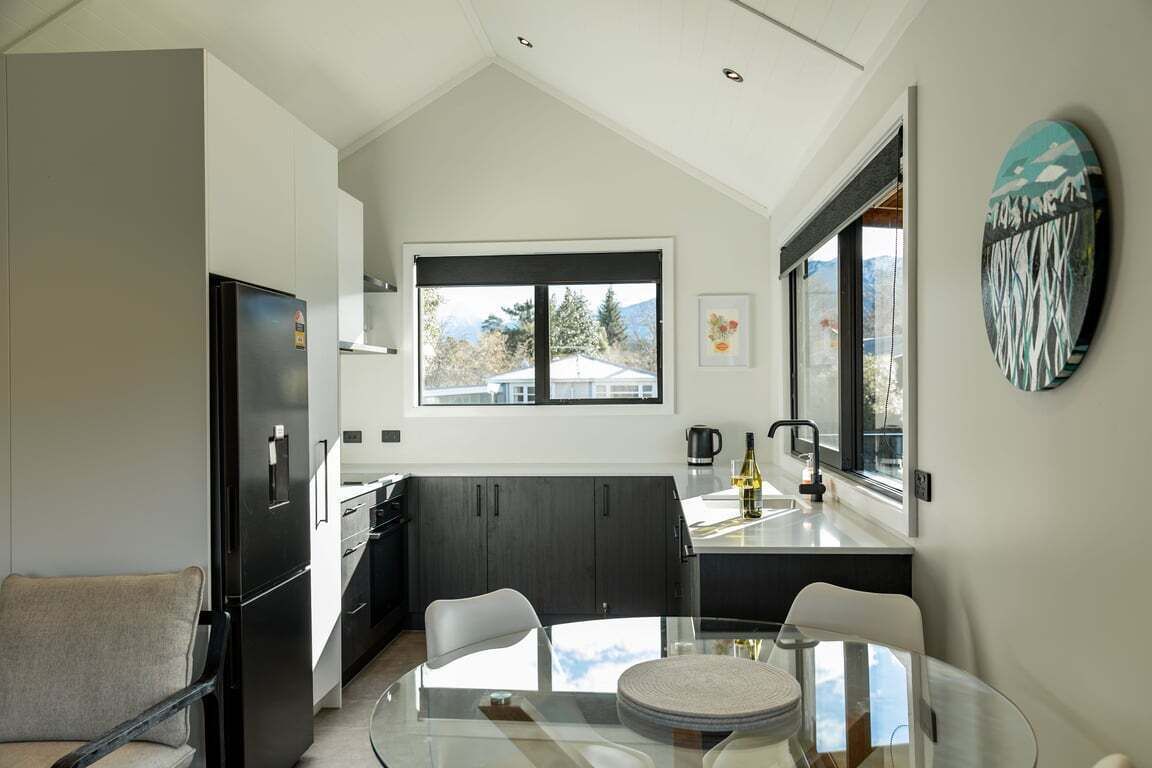 A modern kitchen with a glass dining table, dark cabinets, and a window with a mountain view.