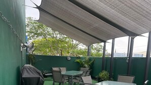 An outdoor patio with a table and chairs, a grill, and a covered area with a fan.
