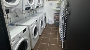 A laundry room with multiple washing machines, a sink, and a trash bin.