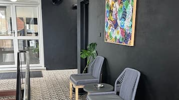Et receptionsområde med moderne design, med en sort væg, et farverigt abstrakt maleri, to grå polstrede stole, et lille rundt bord og et mønstret gulv.