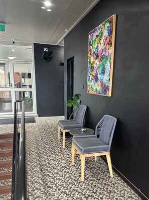 A reception area with a modern design, featuring a black wall, a colorful abstract painting, two grey upholstered chairs, a small round table, and a patterned floor.